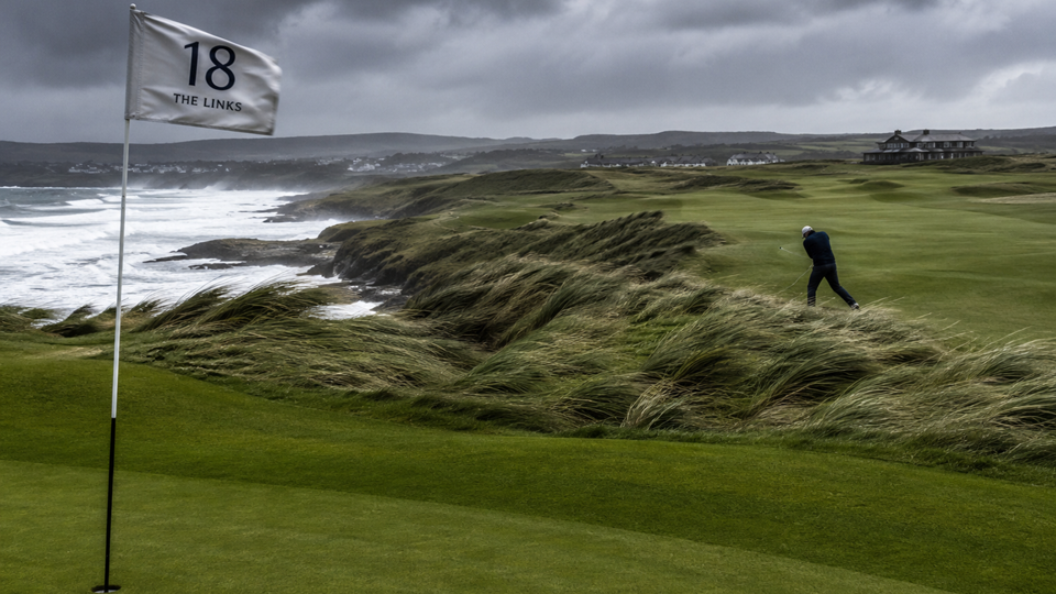 A windy golf course with a flag labelled 18 and a golfer in the background.
